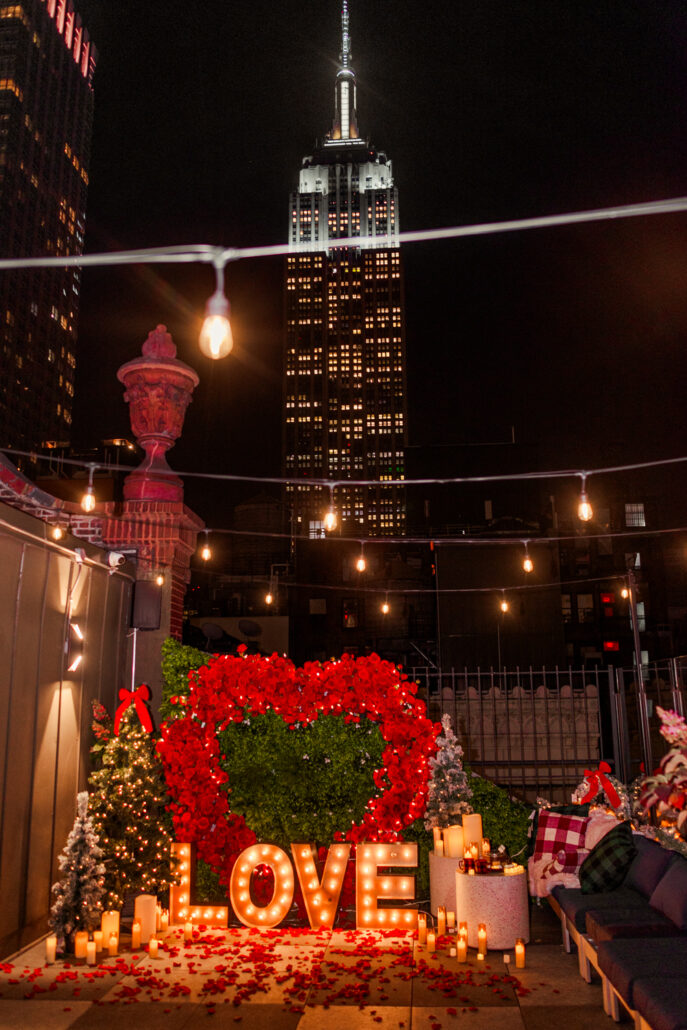 NYC Christmas themed marriage proposal planning in NYC on a private rooftop with a Giant heart and Christmas trees and Empire views 