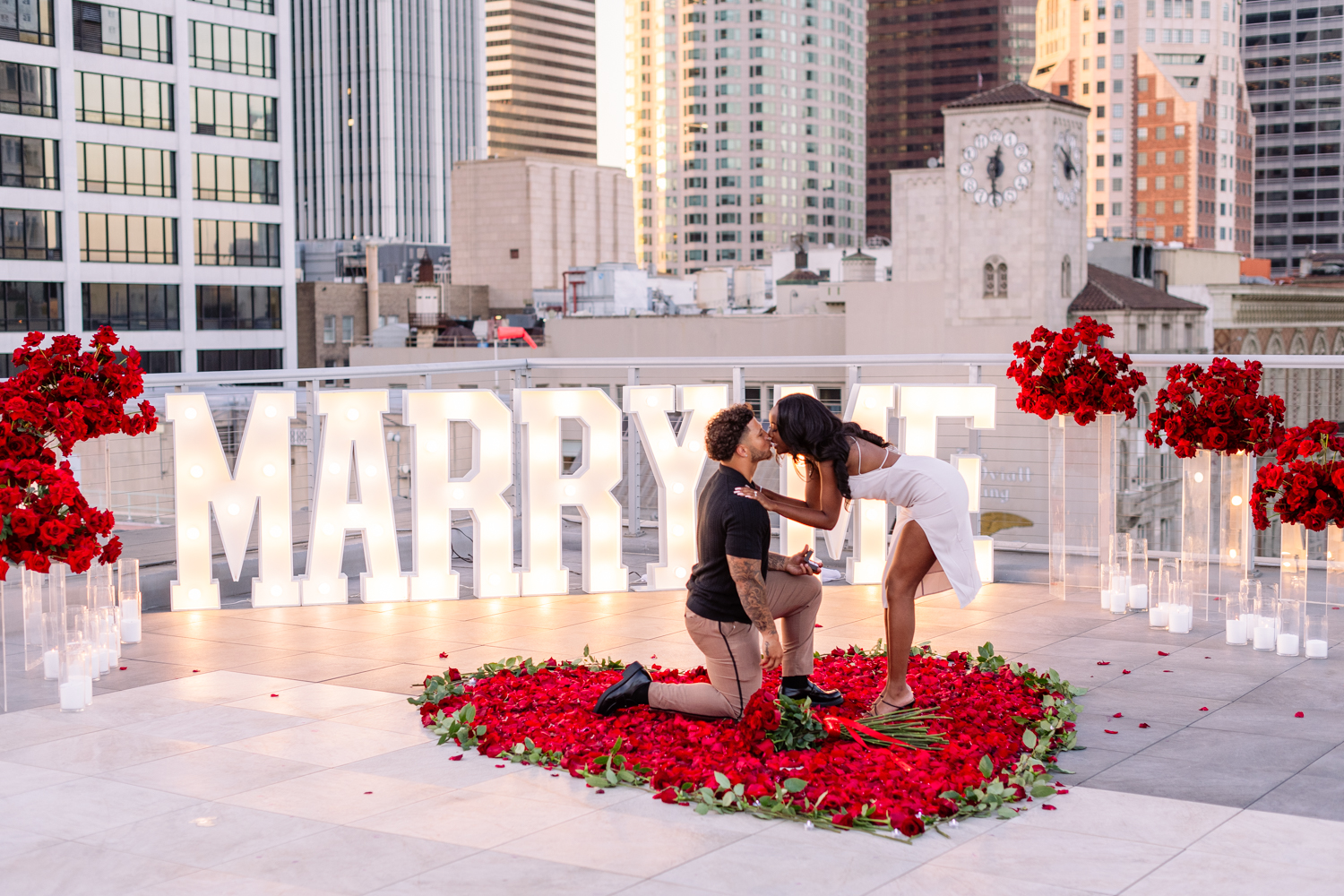 Couple proposing during their LA rooftop proposal with city skyline in the background