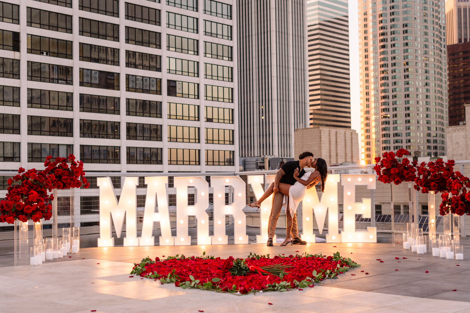 Couple kissing during their LA rooftop proposal with city skyline in the background