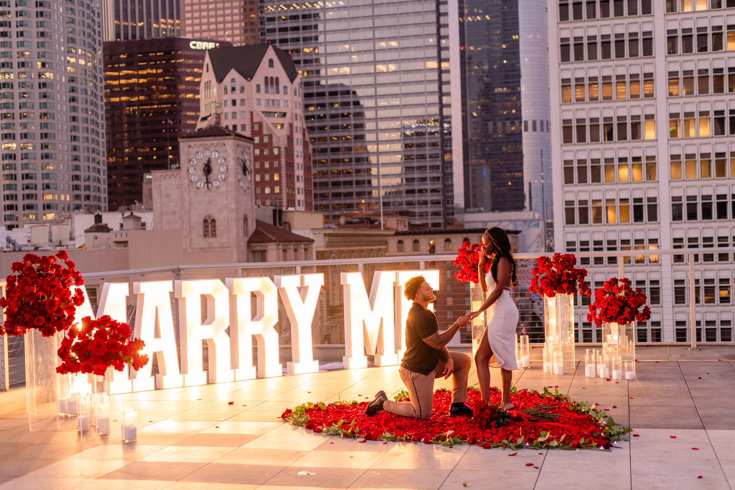 Blake proposing to Makiah during their LA rooftop proposal with city skyline in the background